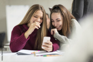 Happy teenage girls in class looking at cell phone
