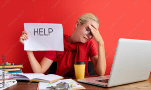 young blonde sad and depressed caucasian manager working in stress at office computer desk feeling overwhelmed and frustrated suffering headache and depression isolated over red background.