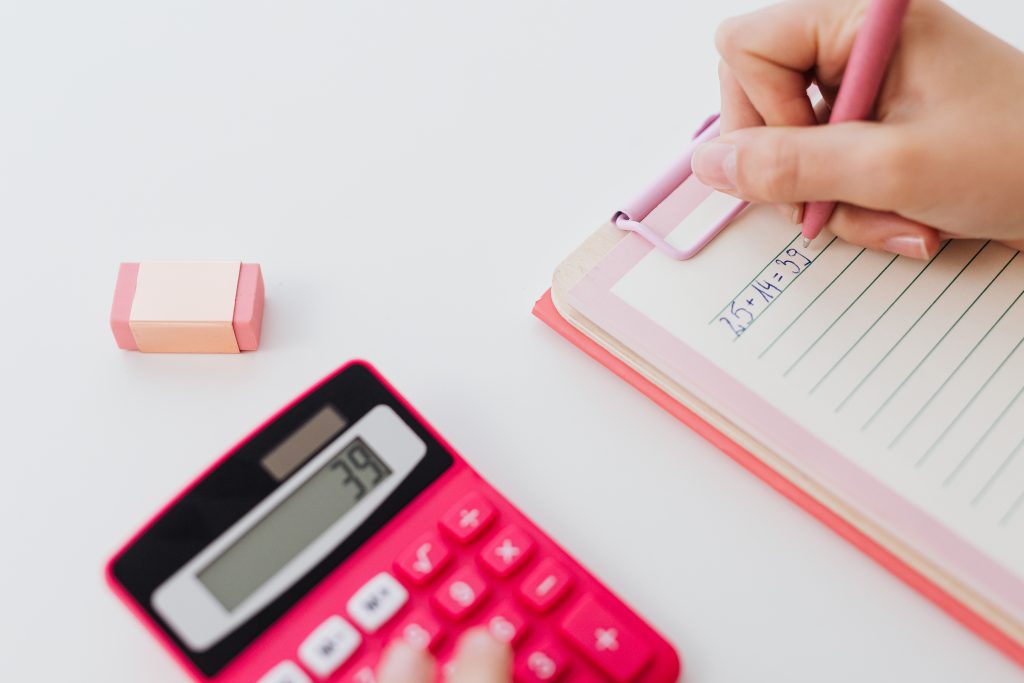 Close up photo of person writing on paper beside calculator