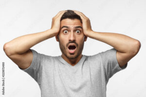 Shock content. Surprised young male in gray t-shirt shouting, holding his head with both hands