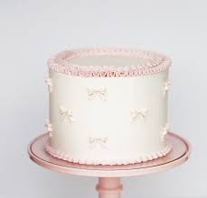 A light pink round cake decorated with small, evenly spaced white bow designs, displayed on a white plate with a light background