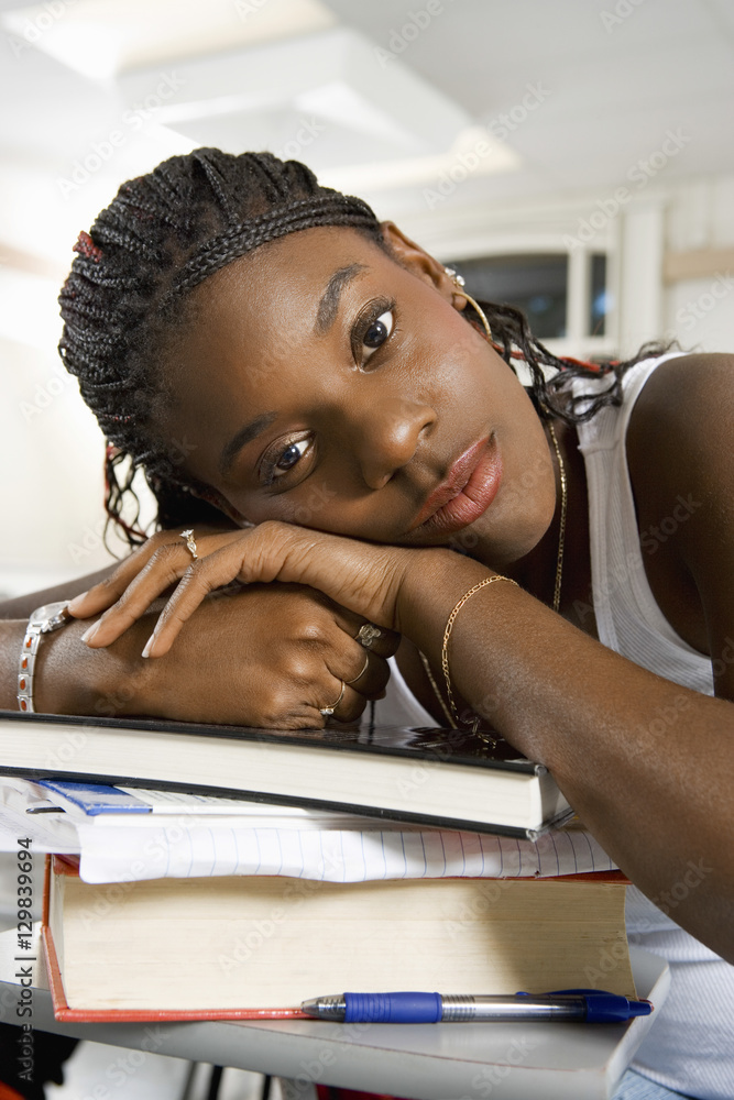Bored young African American woman resting on stack of books in classroom