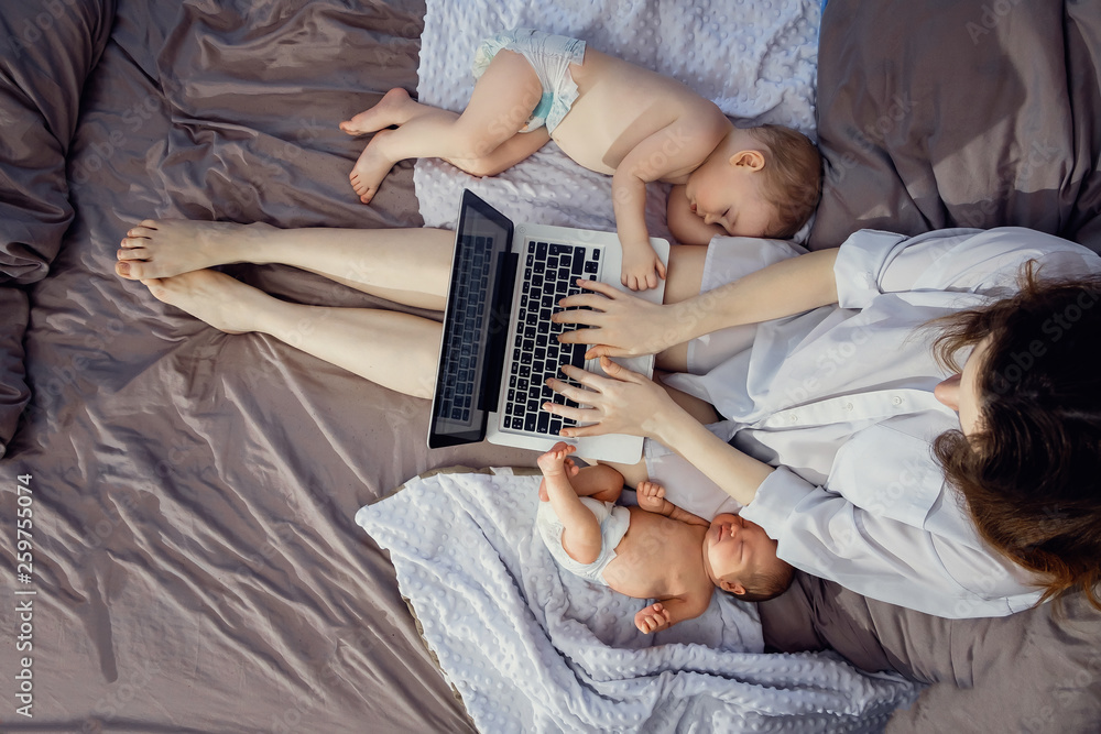 Young beautiful mother freelancer with two children working on a laptop. Freelance, work at home