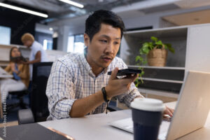 Using smartphone for voice command, man working on laptop in office