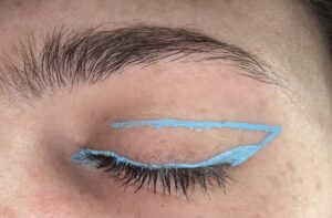 Close up of closed eye. Bright blue liner along the upper lash line and making a wing. At the end of the wing, there is a line straight across to the inner eye. 