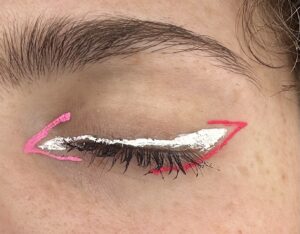 Close up of closed eye. White wing along upper lash line. light pink less than symbol on inner corner. Hot pink line following wing and eye on outer corner.