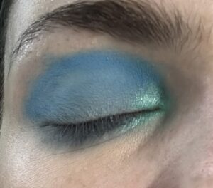 Close-up of closed eye. Light blue lid, blue crease, with a light green, shimmer, inner corner. 