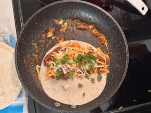 Birria taco assembling and cooking in pan.