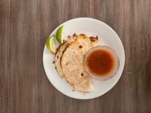 Birria taco served with sauce and lime wedges.