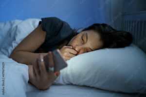 Young anxious asian woman lying in bed staring at smartphone screen at night, reading about depression symptoms in internet, phone addicted female can not stop scrolling social media before bedtime