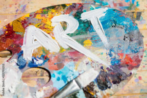 Word art painted with white gouache on colorful palette with paintbrush near by