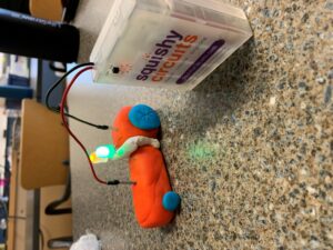 A firetruck made of playdough and plasticine attached to a battery that provides the lights on top with electricity