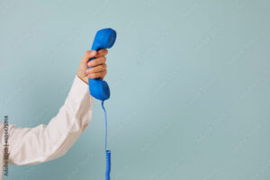 Human hand holding retro phone receiver against copy space background. Cropped shot of young man holding blue landline telephone receiver on light blue copyspace background. Customer support concept