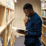 Young black man choosing book in public library