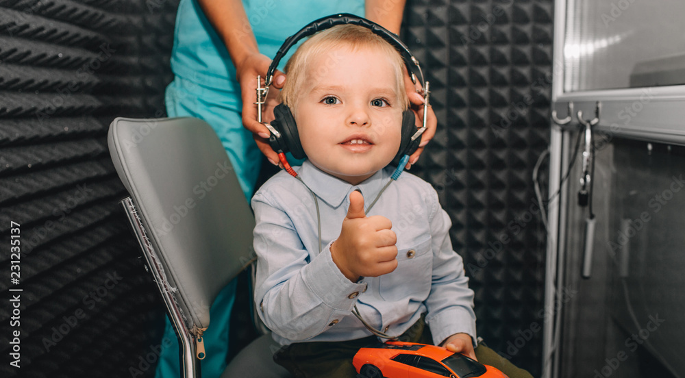 little boy during the hearing exam, showing thumbs up at the audiologist's office. audiogram, children ear exam