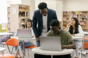 Image of a teacher helping students with their work on computers.