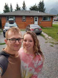 Husband & wife standing in front of log cabin in Banff Alberta 