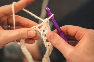 Person holding purple crochet hook and white yarn