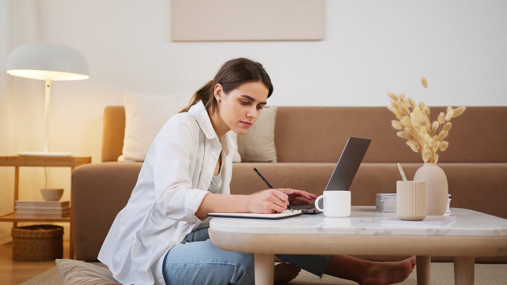 Young woman using laptop and taking notes