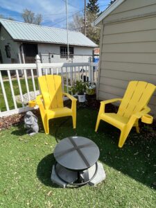 Unplanted hydrangea bush behind firepit and two yellow chairs