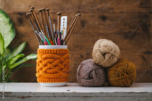 Jar with knitted cover holding different sized knitting needles and crochet hooks.