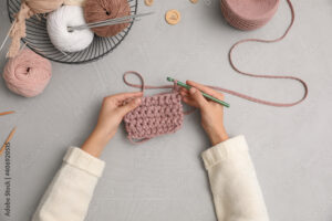 Woman crocheting with threads at grey table, top view. Engaging hobby