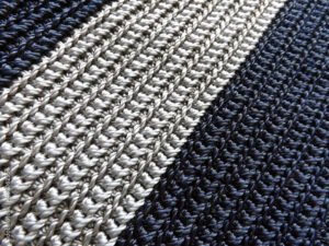 Crocheted fabric texture of grey and blue yarns. Basic crochet stitches are applied on it. Concept of creativity and craftsmanship. Also can be background.
