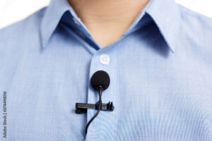 sound recording concept - close up of small lavalier clip-on microphone on blue male shirt