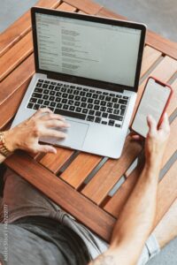 Cropped image of a man using laptop and computer on wooden table