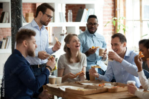 Happy diverse team people talking laughing eating pizza in office