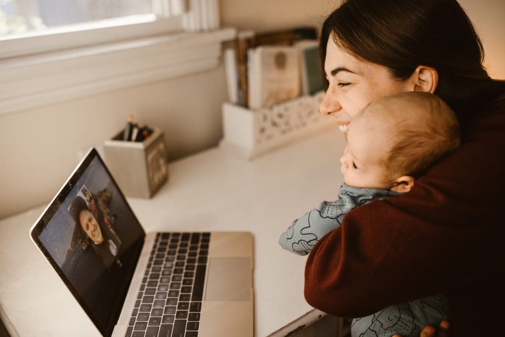 Woman holding her baby while having a video call using a laptop