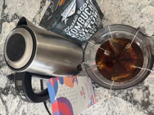 A photograph of 6 bags of black tea steeping in a measuring cup alongside a kettle and package of black tea.