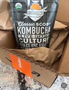 A photo of an open box from Amazon with a black bag package from Fermentaholics with text that reads Classic SCOBY Kombucha Starter Culture.