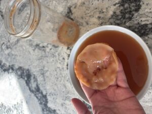 A SCOBY that has been grown from scratch is being held over a bowl of starter tea. In the background is a jar.