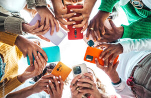 Group of young people using smart mobile phone device outside - Trendy technology concept with guys and girls playing video games app on smartphone - Bright colorful filter