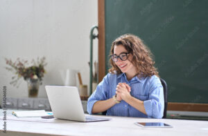 Young happy business woman employee or teacher feeling pleased and excited looking at laptop reading good news online getting salary or career growth, satisfied with great result sitting at work desk.