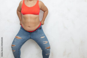 Unrecognizable adipose, fat, obese and overweight woman in red bikini pulling and getting dressed in small size tight jeans, to fit hips in clothes on white background. Preparation summer season