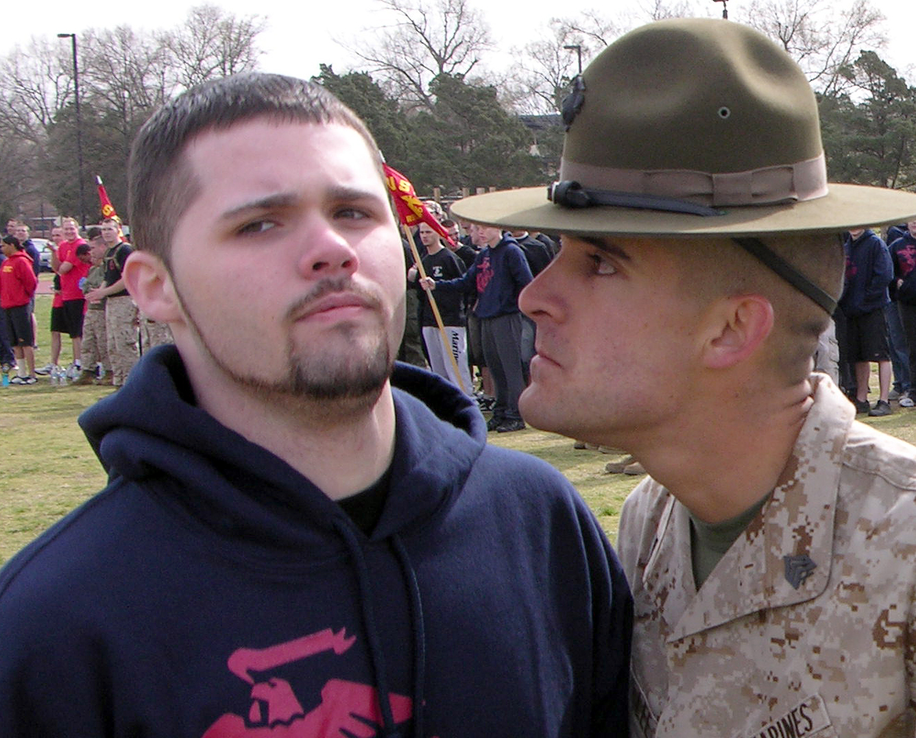 A drill sergeant leans in close towards a young man.