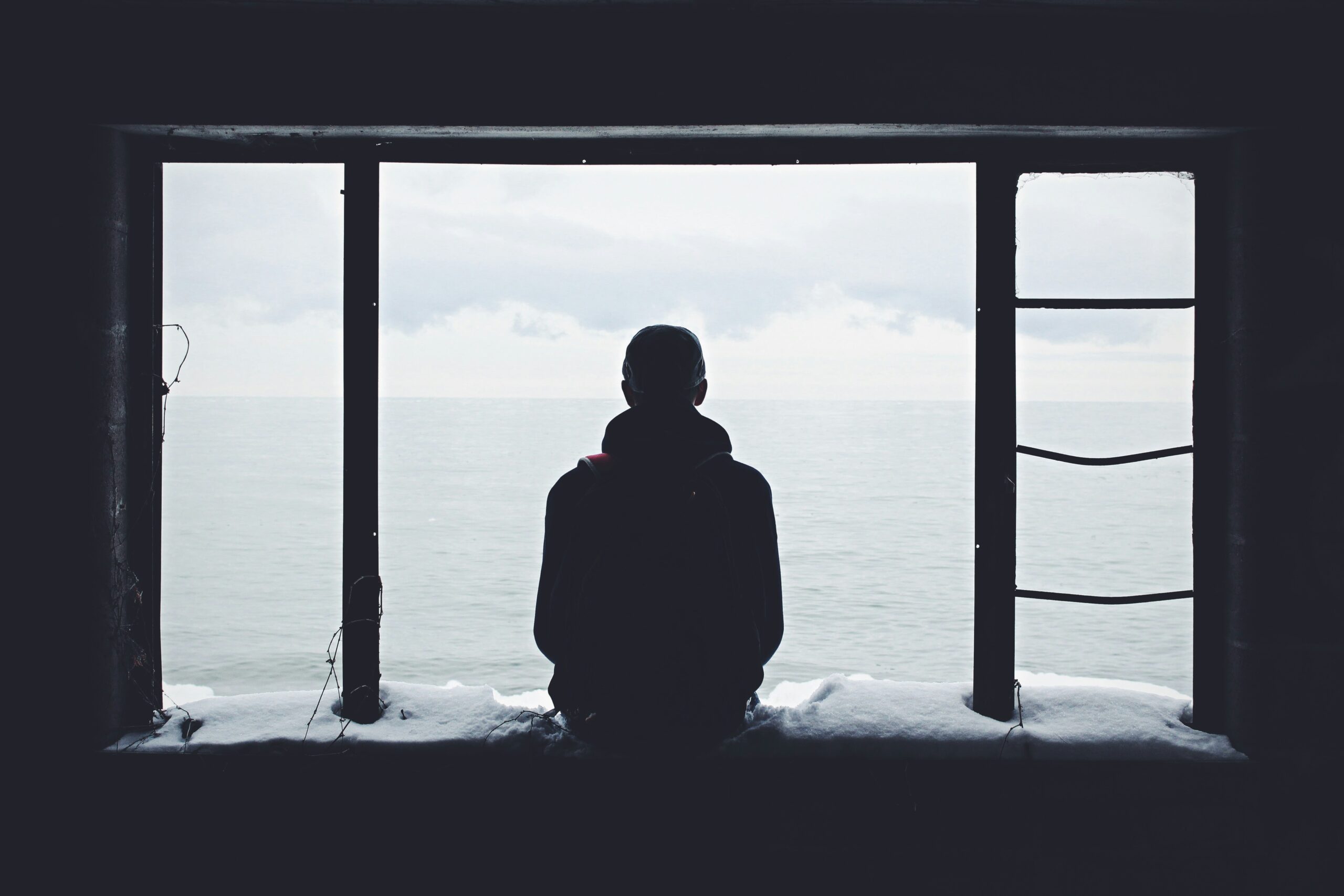 A man sits alone looking out of a window.