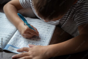 close up top view of boy's hands writing russian cursive letters in a copybook. Image with selective focus