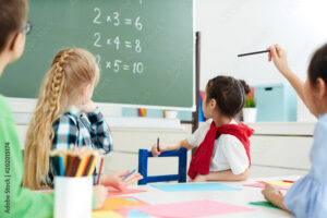 Elementary school kids sitting in classroom and looking at blackboard with multiplication sums