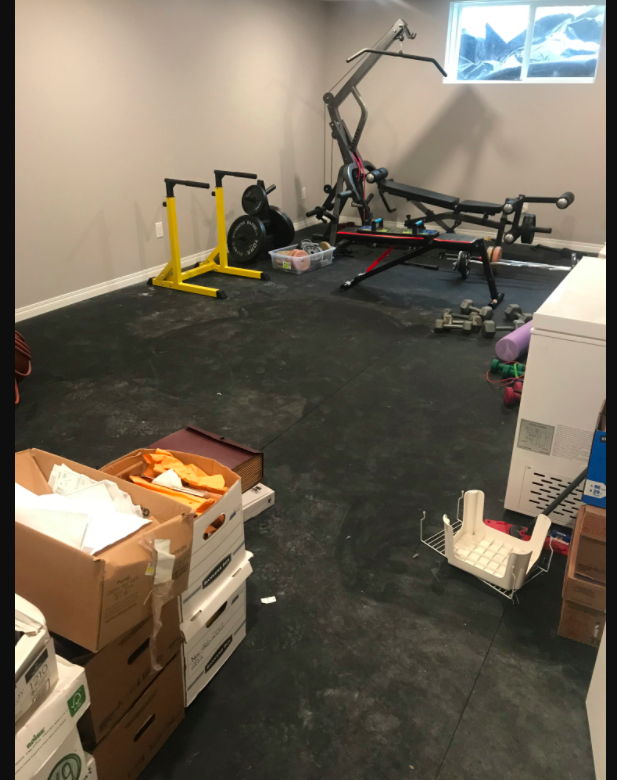 picture of home gym with boxes of paperwork and freezers and dirty floors.