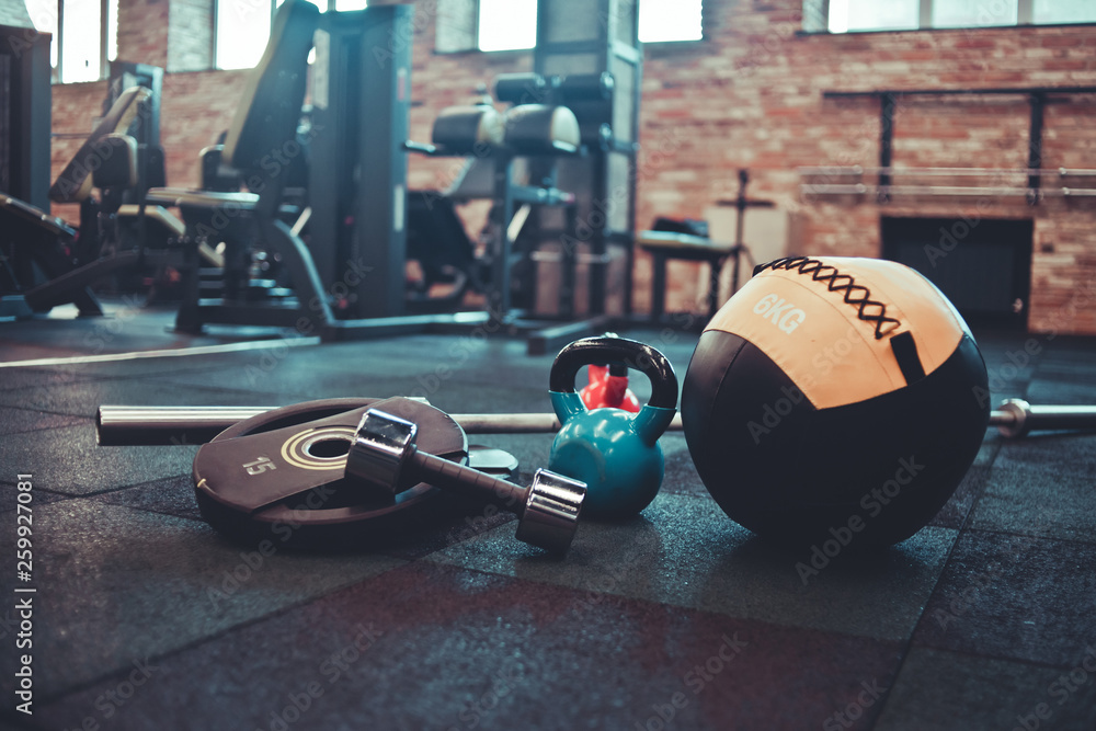 Disassembled barbell, medicine ball, kettlebell, dumbbell lying on floor in gym. Sports equipment for workout with free weight. Functional training