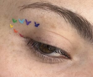Close up of slightly open eye with rainbow hearts along the wing line.