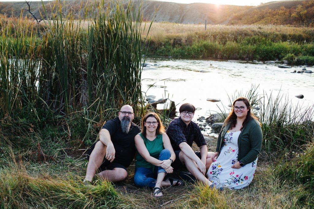 Family sitting in the grass by a river at Wascana Trails