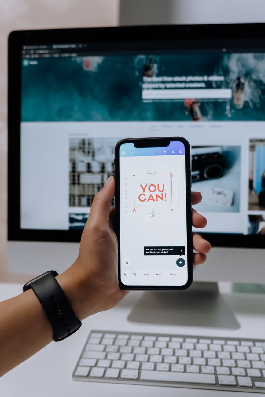 holding a smartphone in front of an imac