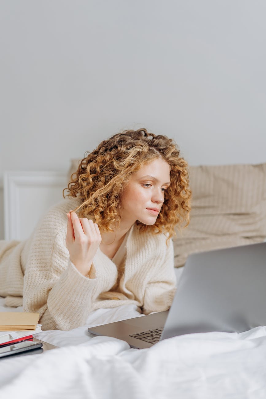 woman lying down on bed looking at her laptop