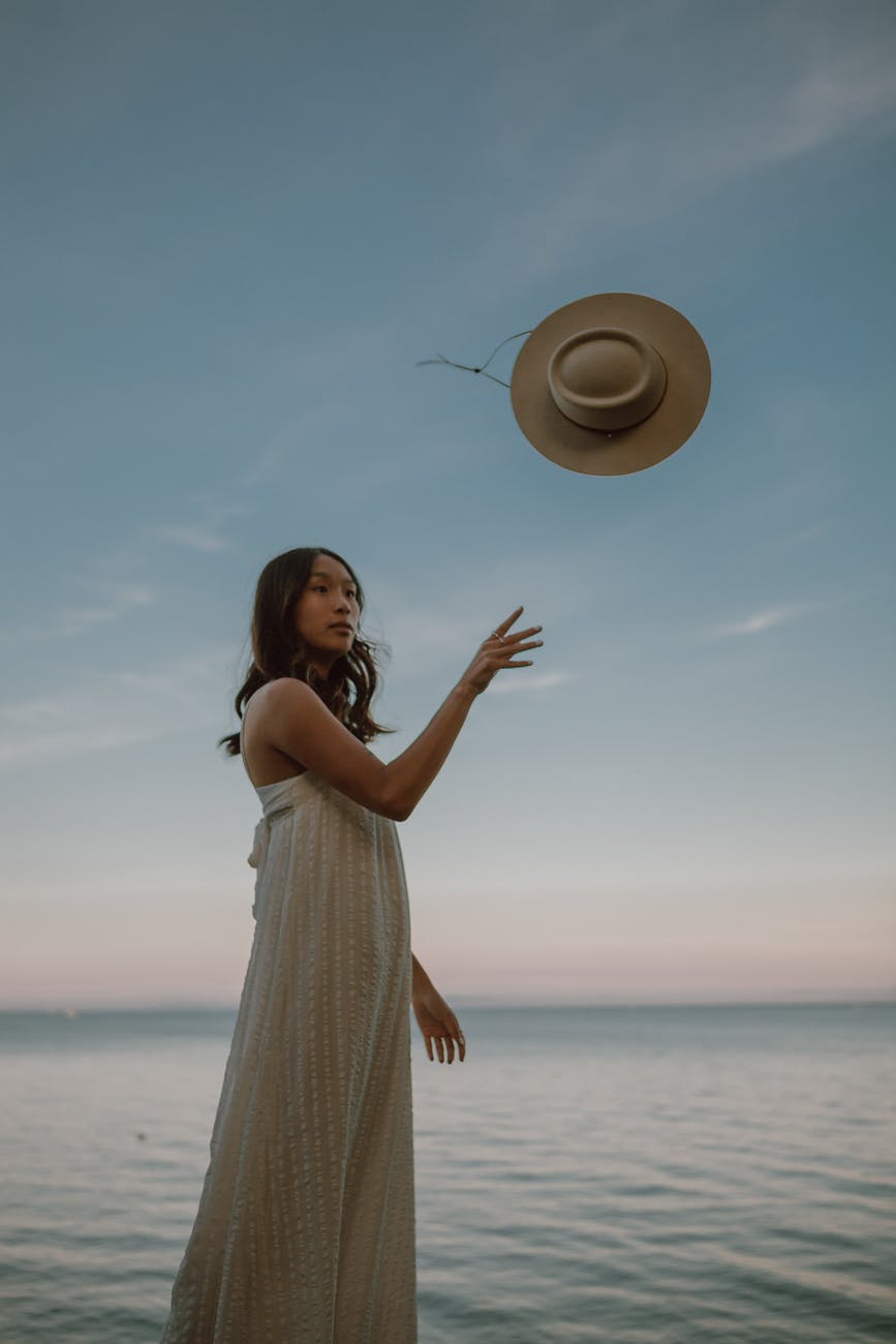 calm ethnic female throwing hat while standing in sea